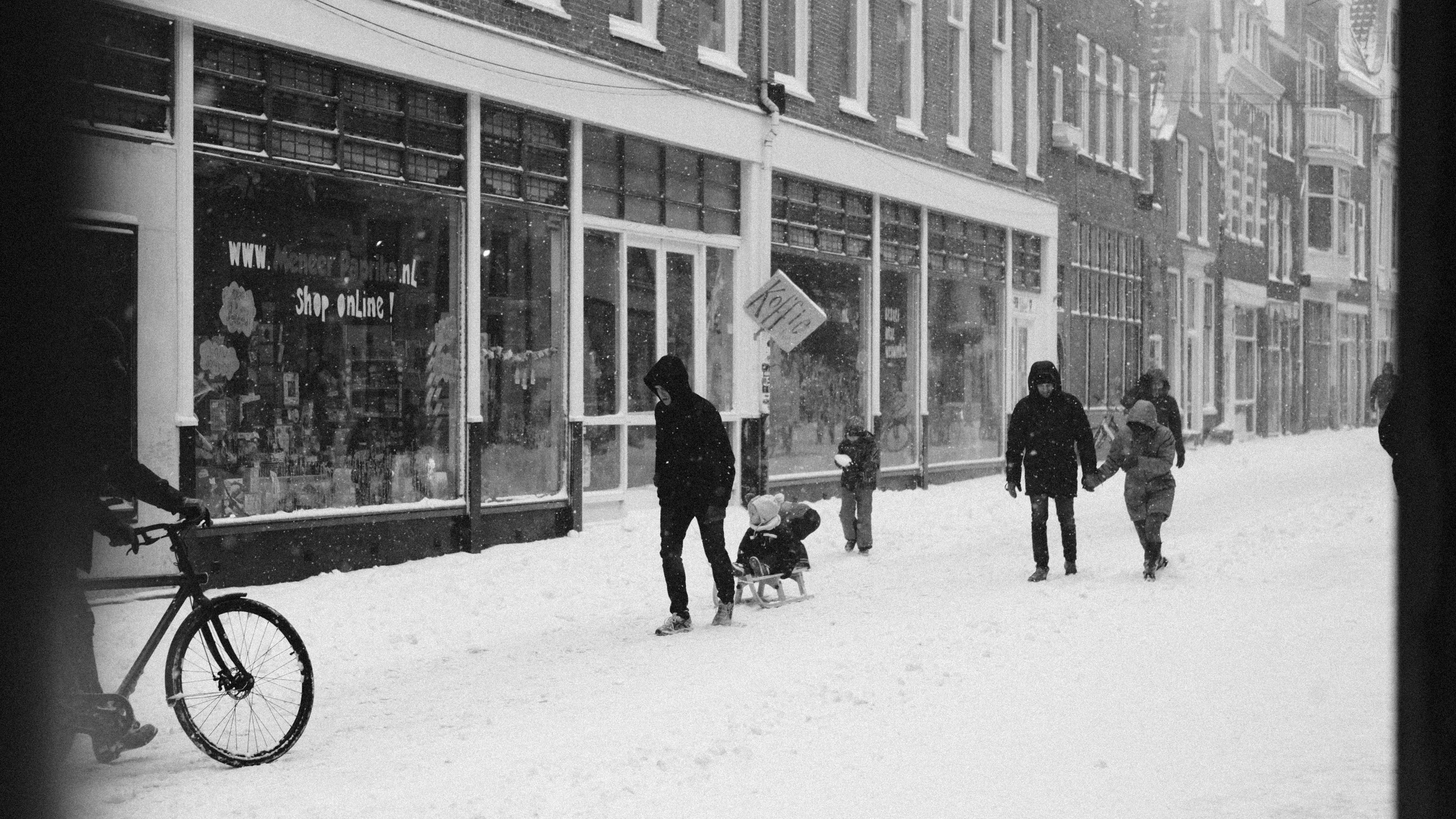 man in black jacket walking with black dog on snow covered ground