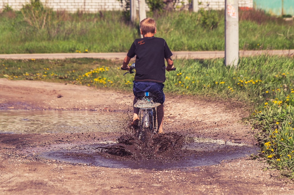boy in black long sleeve shirt riding bicycle on dirt road during daytime