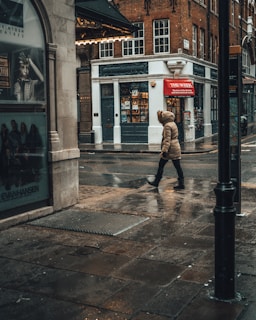 A model walking through a rainy city street wearing layered urbanhikes gear with a hood up.