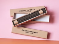 Three rectangular boxes containing Japanese incense sticks are arranged on a pink surface. The boxes are labeled with the brand 'ENCENS JAPONAIS MAISON BALZAC' and have a minimalist design.