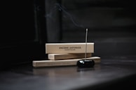 Two rectangular boxes labeled 'ENCENS JAPONAIS' rest horizontally, with a lit incense stick inserted into a black holder in the foreground. Smoke gently rises from the incense, creating a serene and tranquil atmosphere.