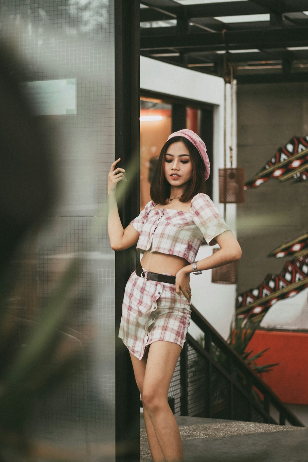 woman in white and pink plaid dress standing beside glass wall