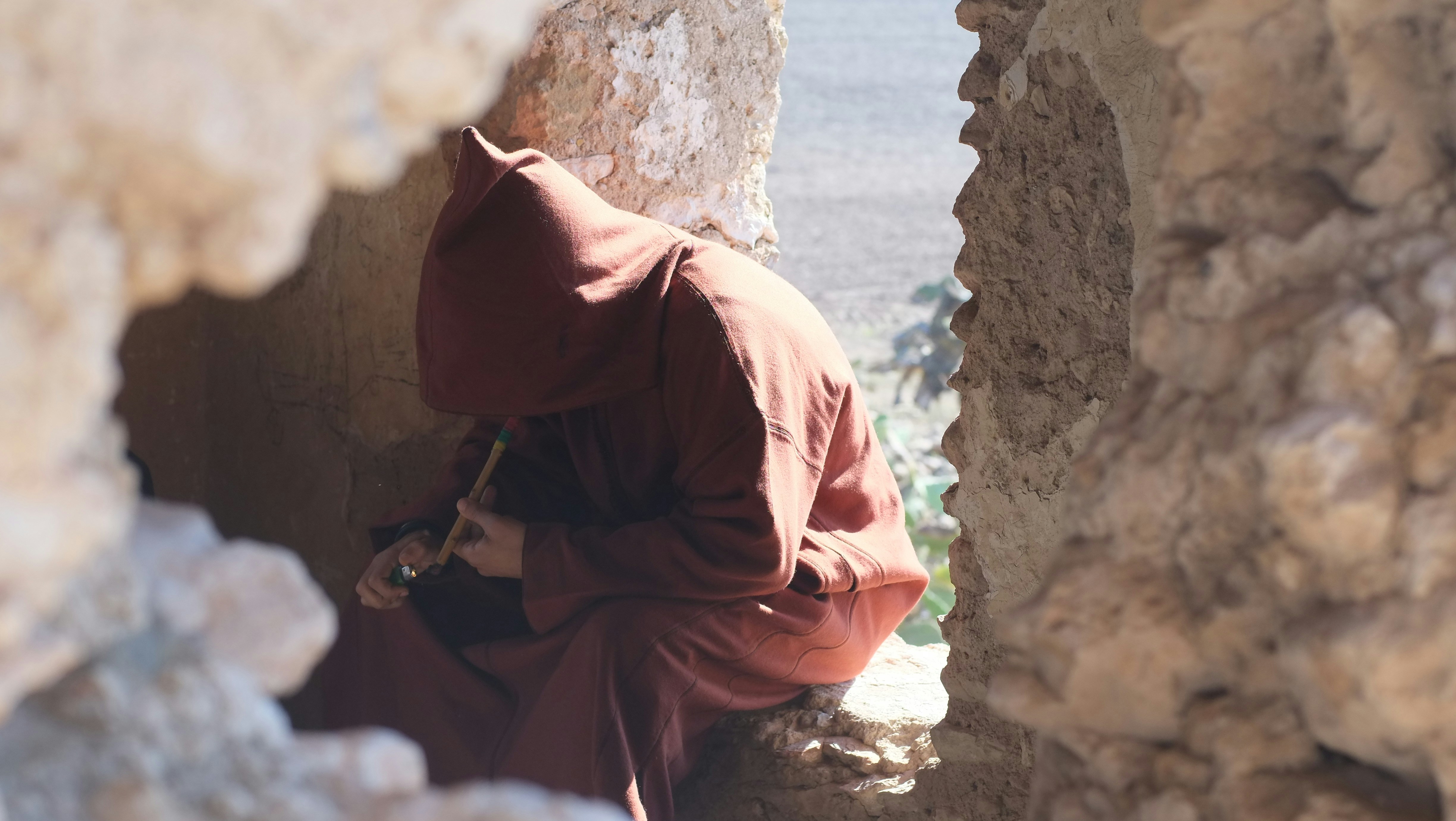 person in brown hijab and black abaya sitting on rock during daytime