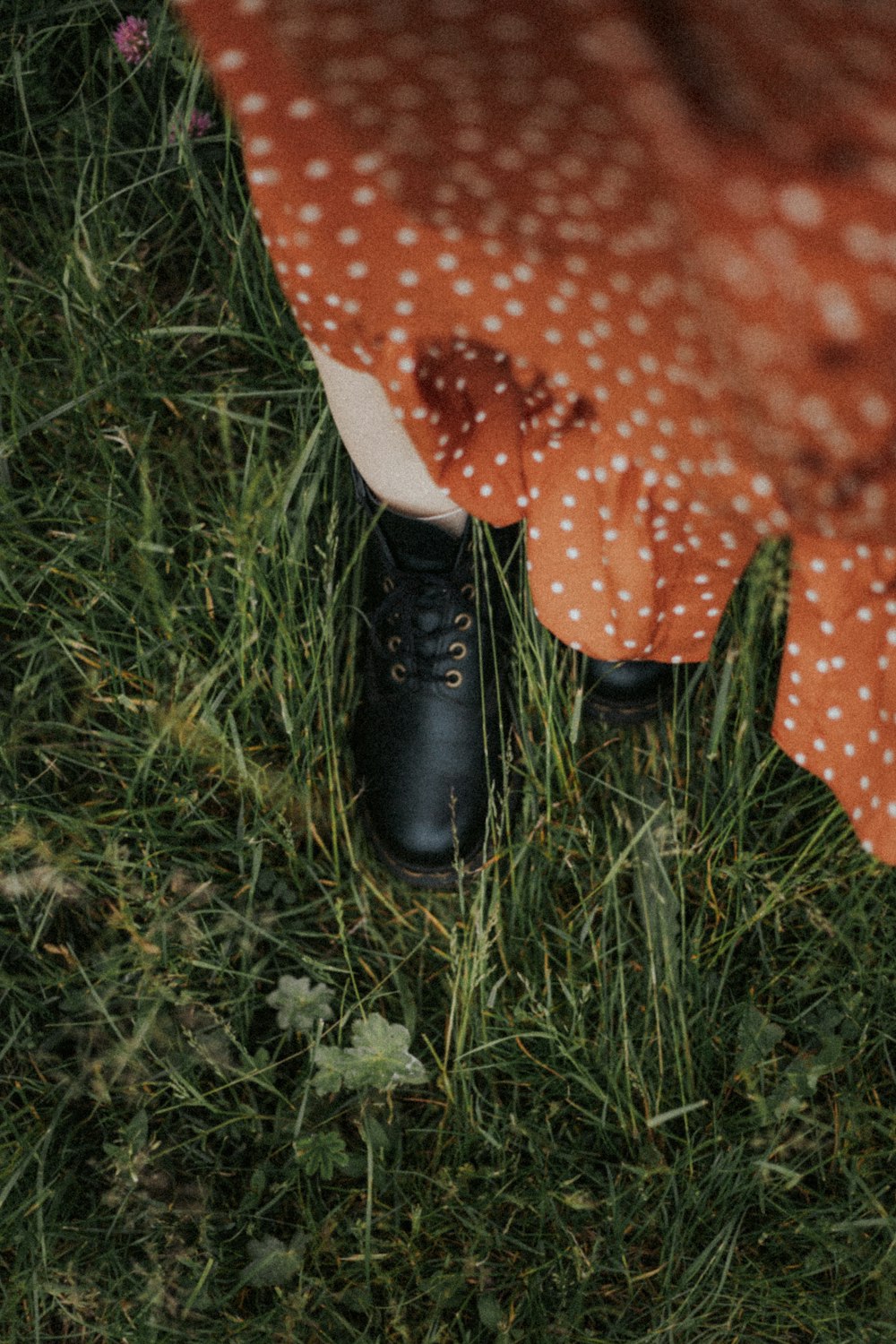 person in red and white polka dot pants and black leather shoes standing on green grass