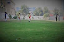 Young campers playing soccer together on a green field with city buildings in the background.