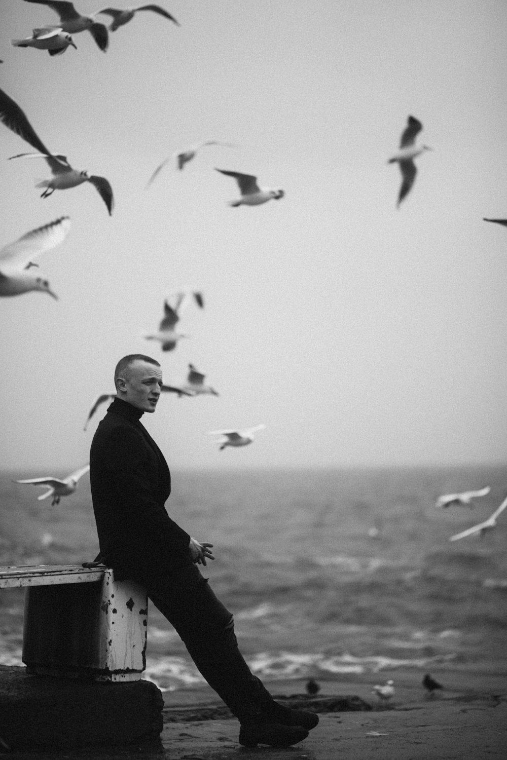 man in black long sleeve shirt standing near birds in grayscale photography