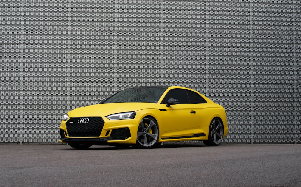 yellow mercedes benz coupe parked beside gray wall