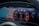A digital car dashboard displays a map with navigation, speedometer, and various gauges. The map shows detailed routes and landmarks. The central tachometer shows RPM with a redline indication and branding. Additional information includes mileage, fuel level, power meter, and temperature.