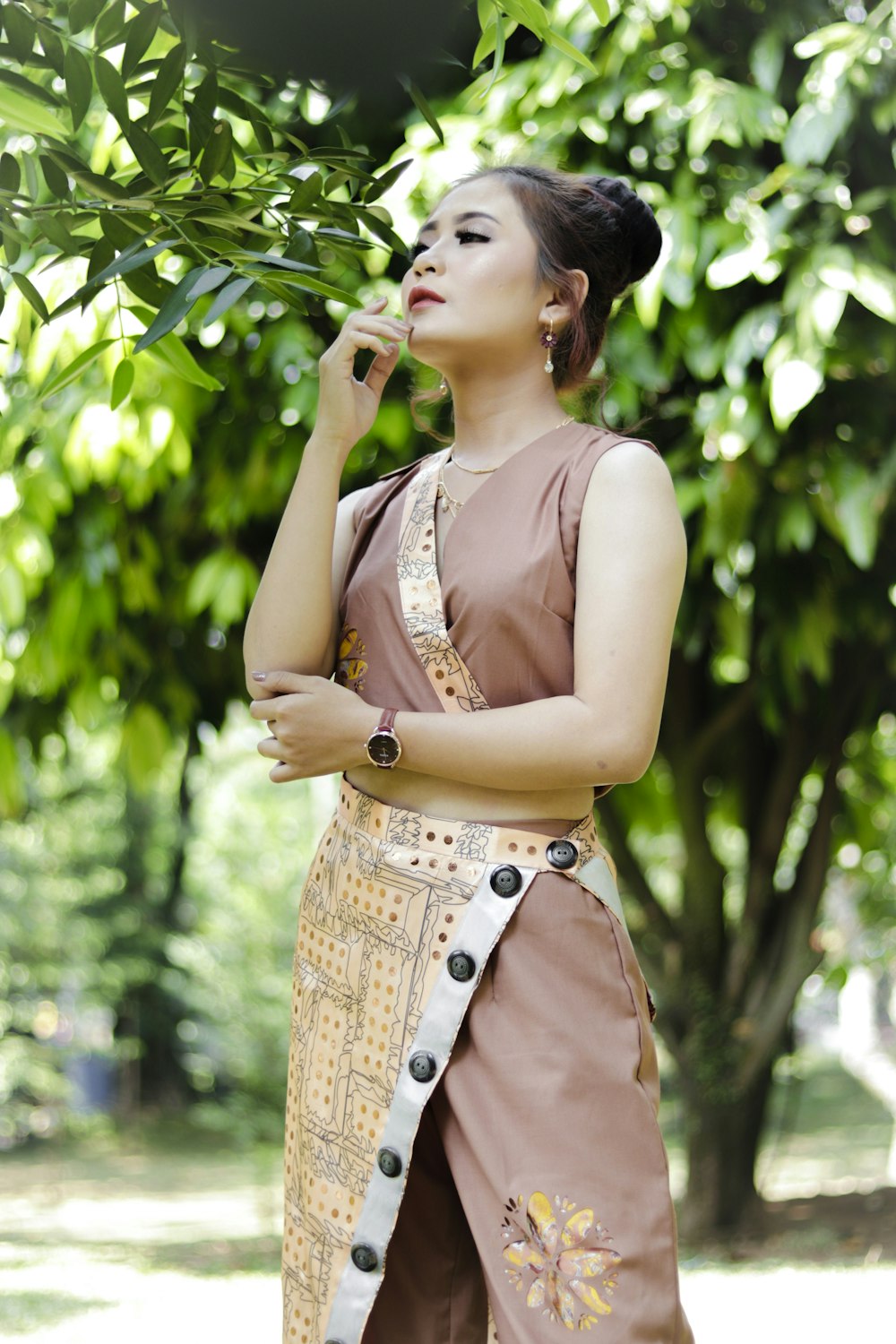 woman in brown tank top and brown denim shorts standing near green leaf tree during daytime