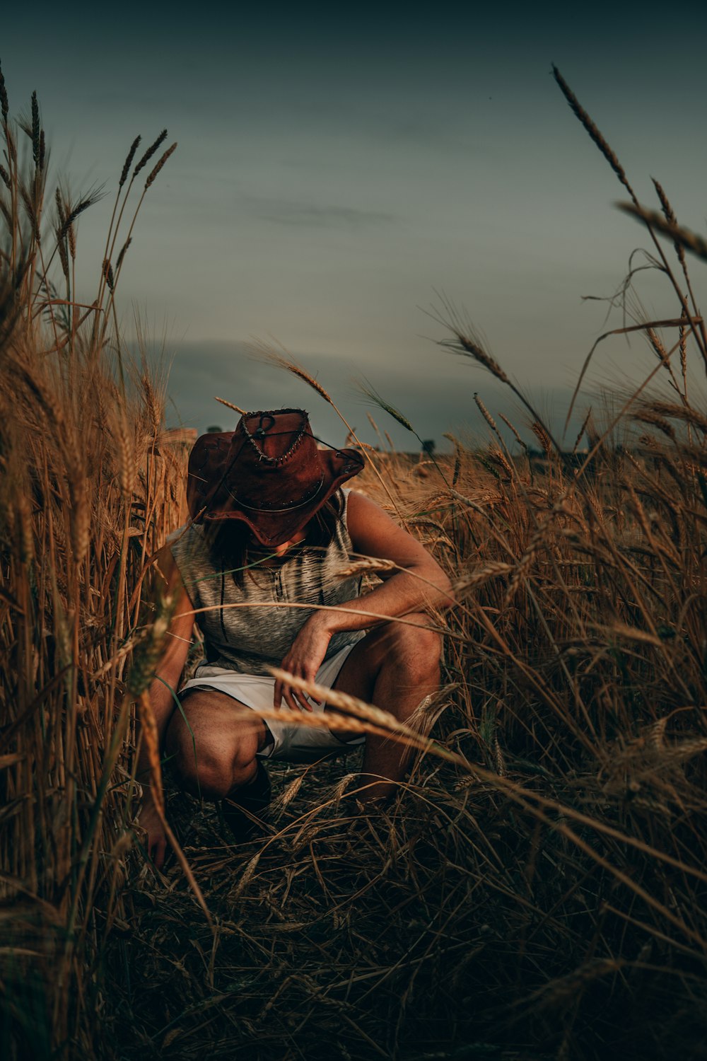 uomo in canotta nera che indossa occhiali da sole seduto sul campo di erba marrone durante il giorno