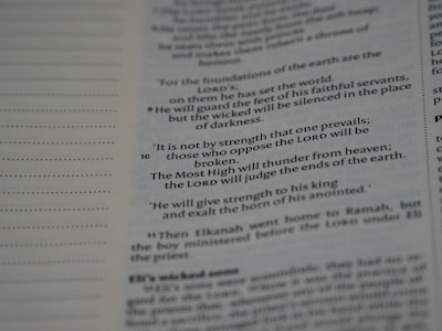 An open page with printed text from a religious book, possibly a Bible, featuring distinct verses and organized lines. The text is black on a white background.