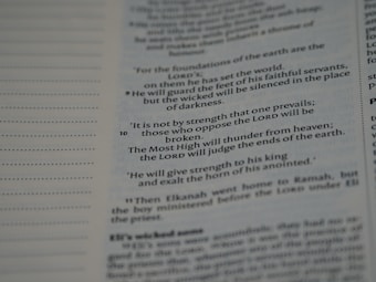 An open page with printed text from a religious book, possibly a Bible, featuring distinct verses and organized lines. The text is black on a white background.