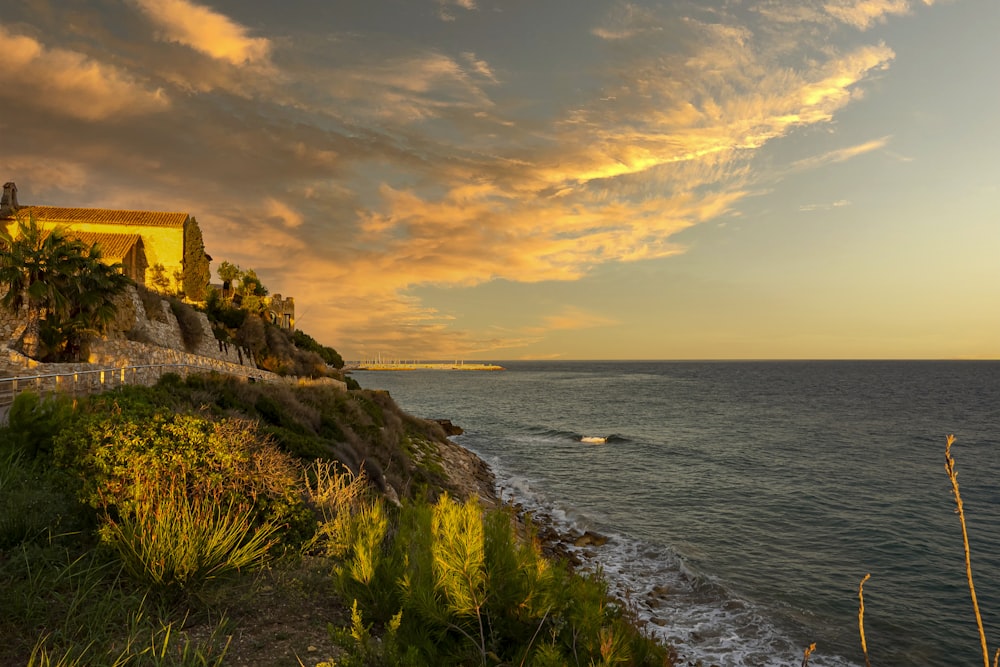 brown concrete building on cliff by the sea during sunset