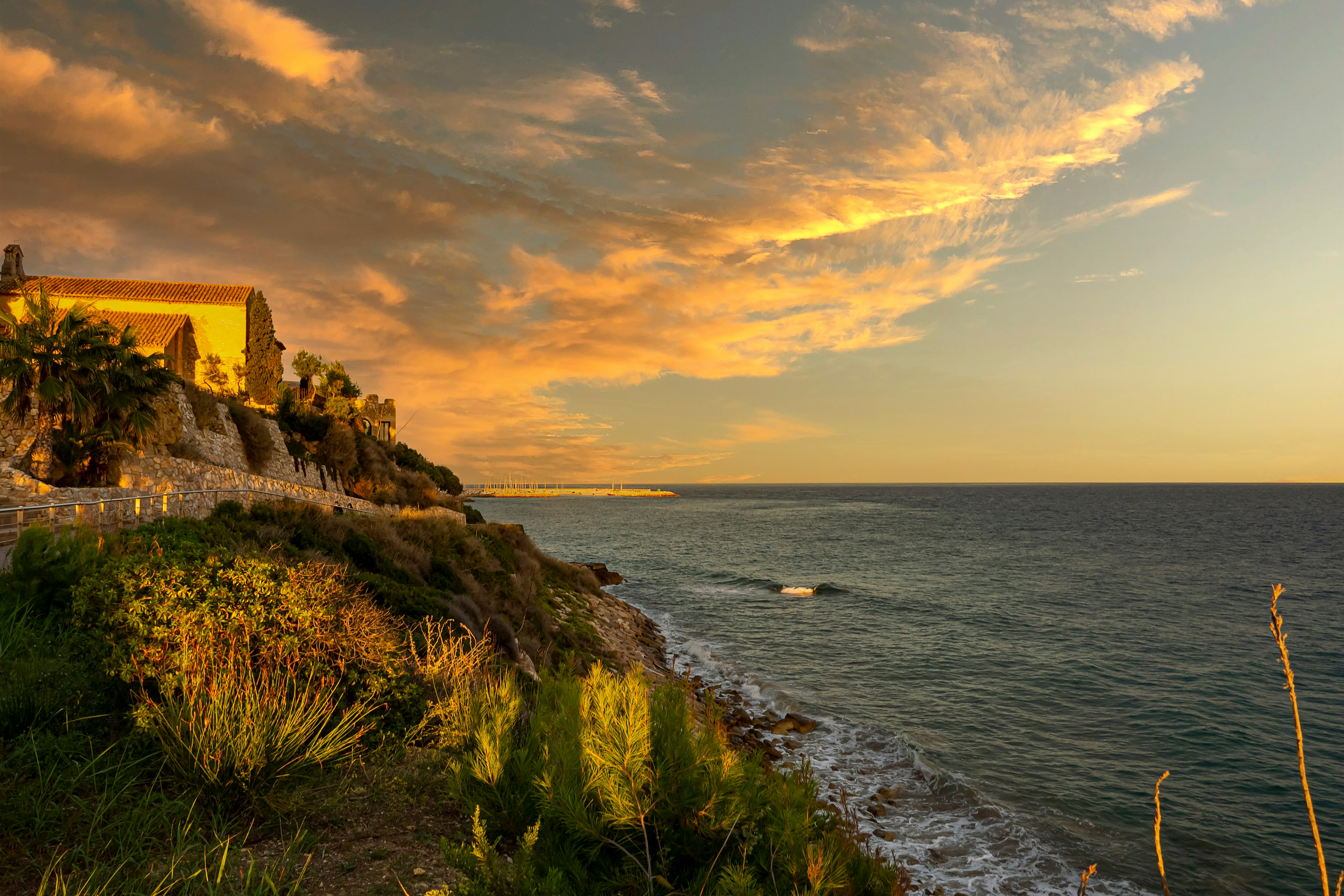 brown concrete building on cliff by the sea during sunset