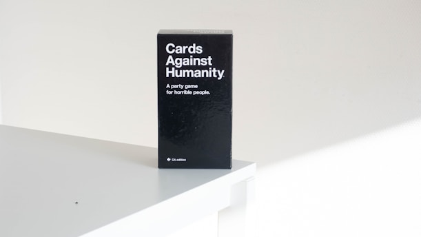 A black box of the card game 'Cards Against Humanity' is placed on a white surface. The text on the box reads 'A party game for horrible people'. The setting appears minimalistic with a focus on the game's packaging.