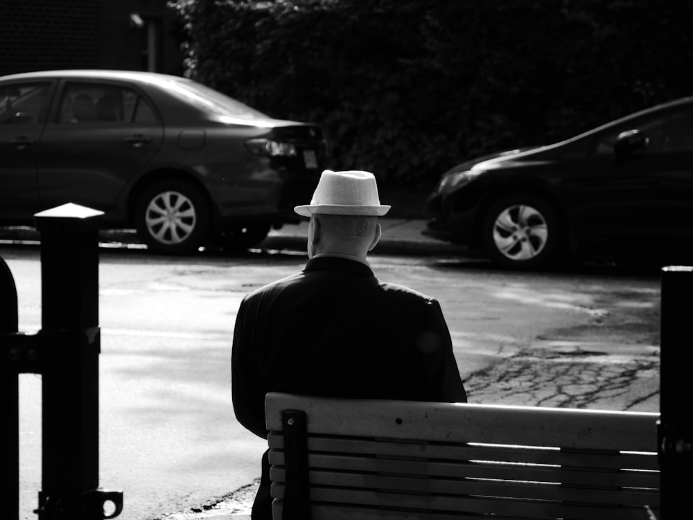 grayscale photo of man wearing hat sitting on bench