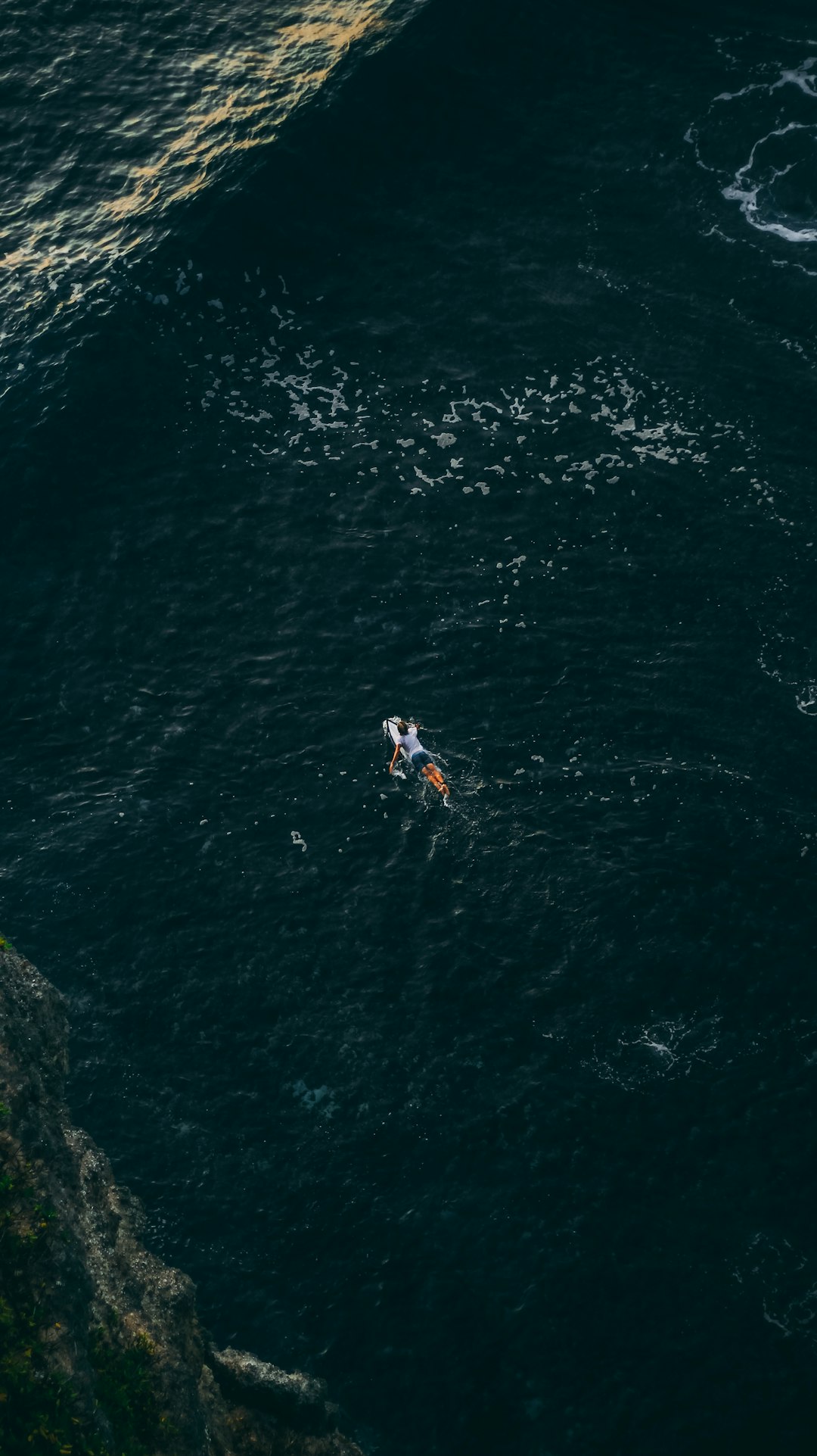 person in white shirt and blue shorts standing on rock formation beside body of water during