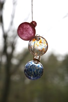Hand-painted glass balls hanging from a branch, showcasing delicate dot painting designs.