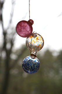 Hand-painted glass balls hanging from a branch, showcasing delicate dot painting designs.