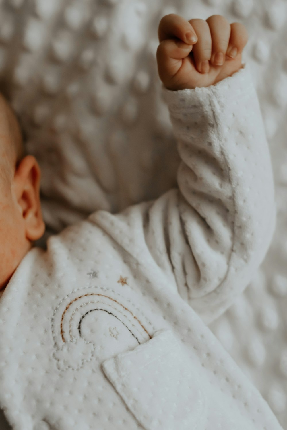 baby in white onesie lying on white textile