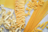 Variety of dried pasta shapes arranged neatly on a cream-colored surface.
