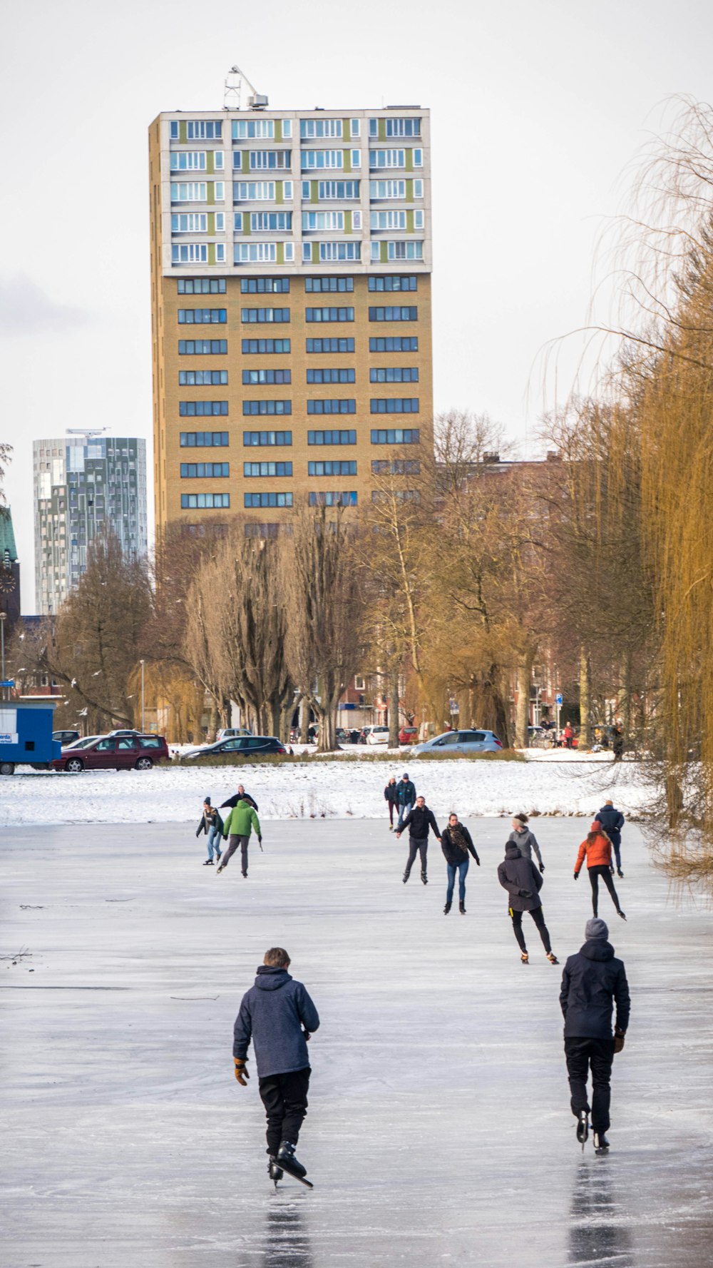people playing ice hockey on snow covered field near high rise building during daytime