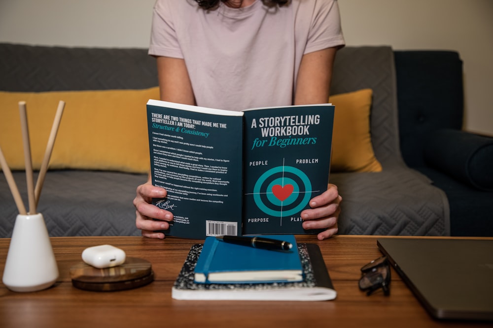 man in white crew neck t-shirt holding blue book