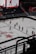 A group of hockey players in red uniforms are practicing or preparing for a game on an indoor ice rink. The arena is mostly empty, with a few spectators visible in the stands. A large digital screen displays images of players on the ice. The ice surface is marked with team logos and advertisements.