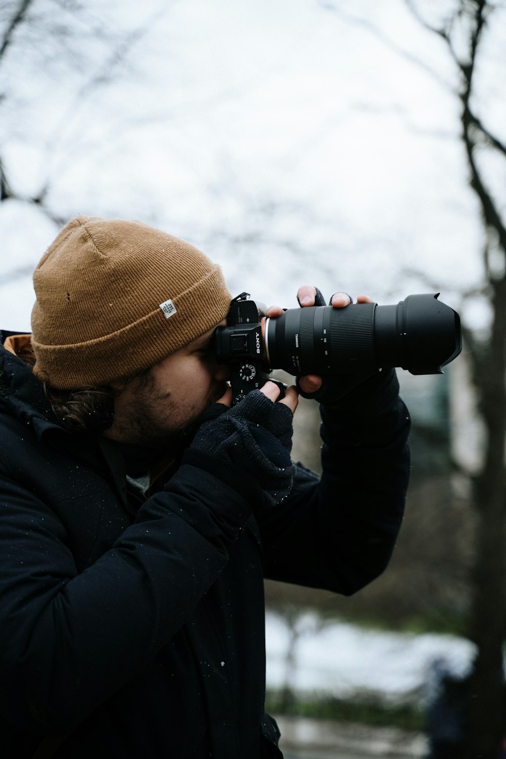 검은 색 자켓과 검은 색 DSLR 카메라를 사용하는 갈색 니트 모자를 쓴 남자