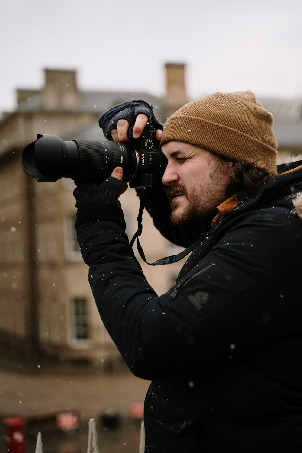 man in black jacket and brown knit cap holding black dslr camera