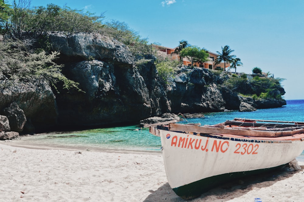 barco branco e vermelho na praia durante o dia