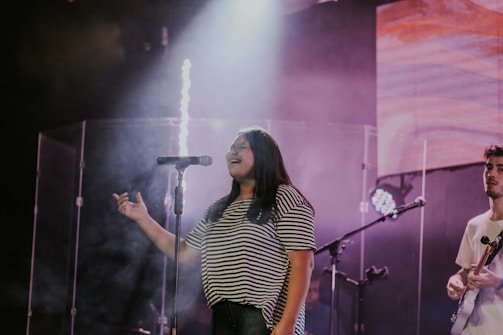 woman in black and white stripe shirt singing on stage