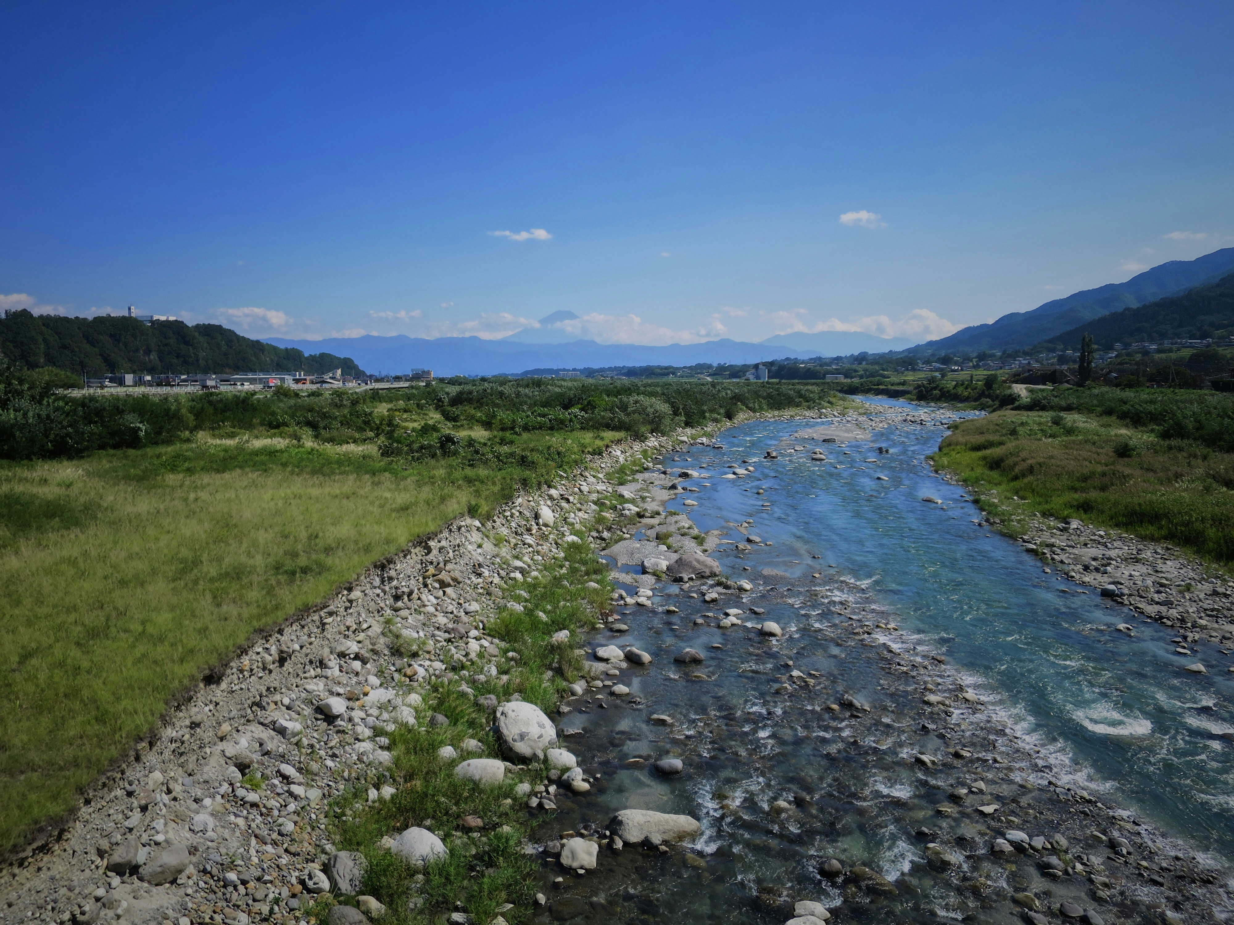 green grass field near river under blue sky during daytime