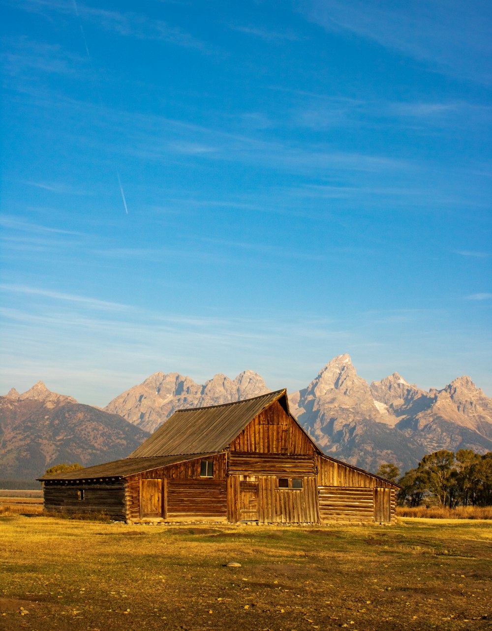 brown wooden house on brown grass field near mountain under blue sky during daytime
