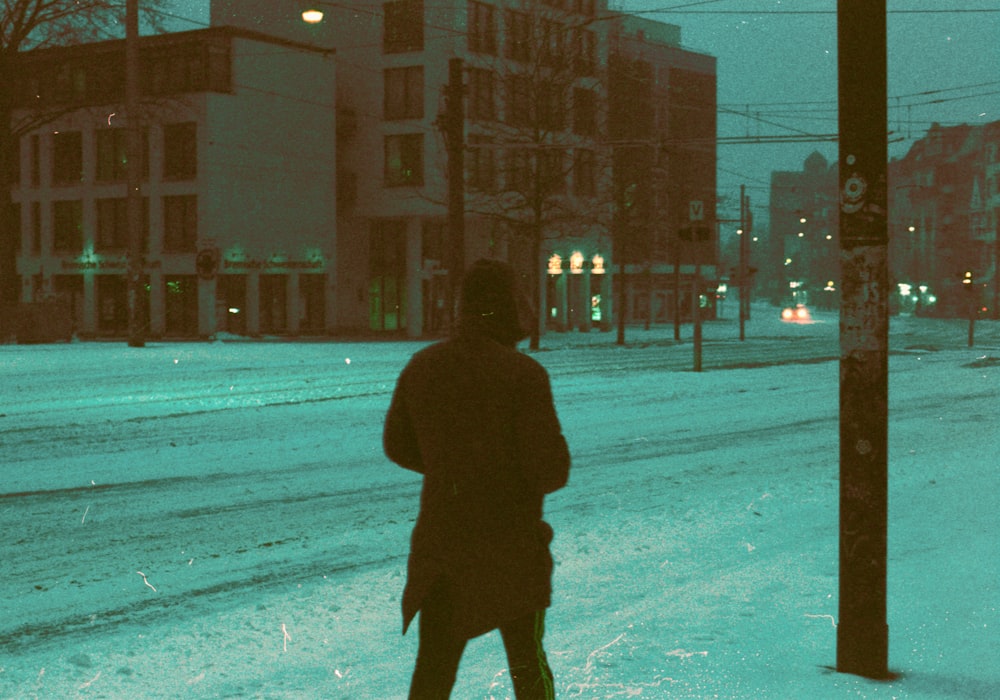 personne en manteau noir marchant sur une route enneigée pendant la journée