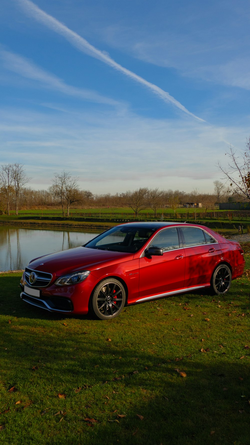 red sedan parked on green grass field near body of water during daytime