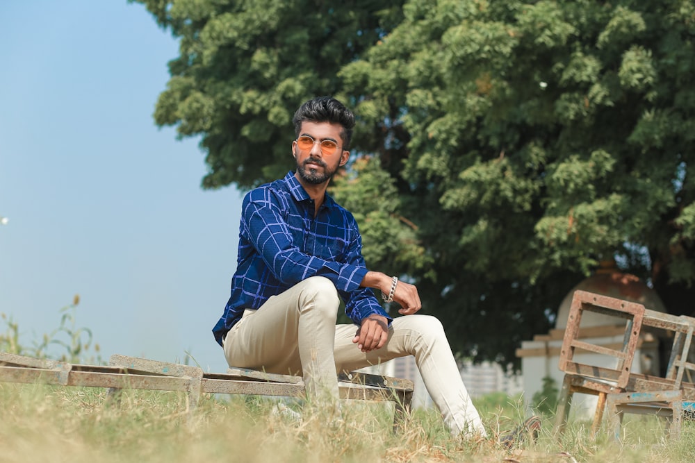 man in blue and white plaid dress shirt sitting on brown wooden fence during daytime