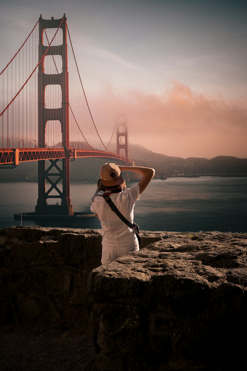 woman in white shirt and white pants sitting on rock near golden gate bridge during daytime