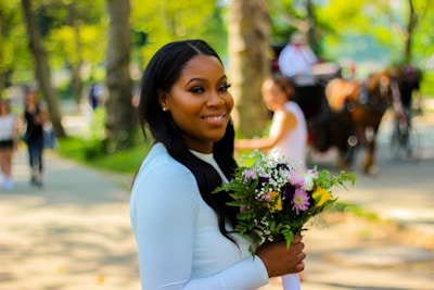 smiling woman in white long sleeve shirt holding bouquet of flowers