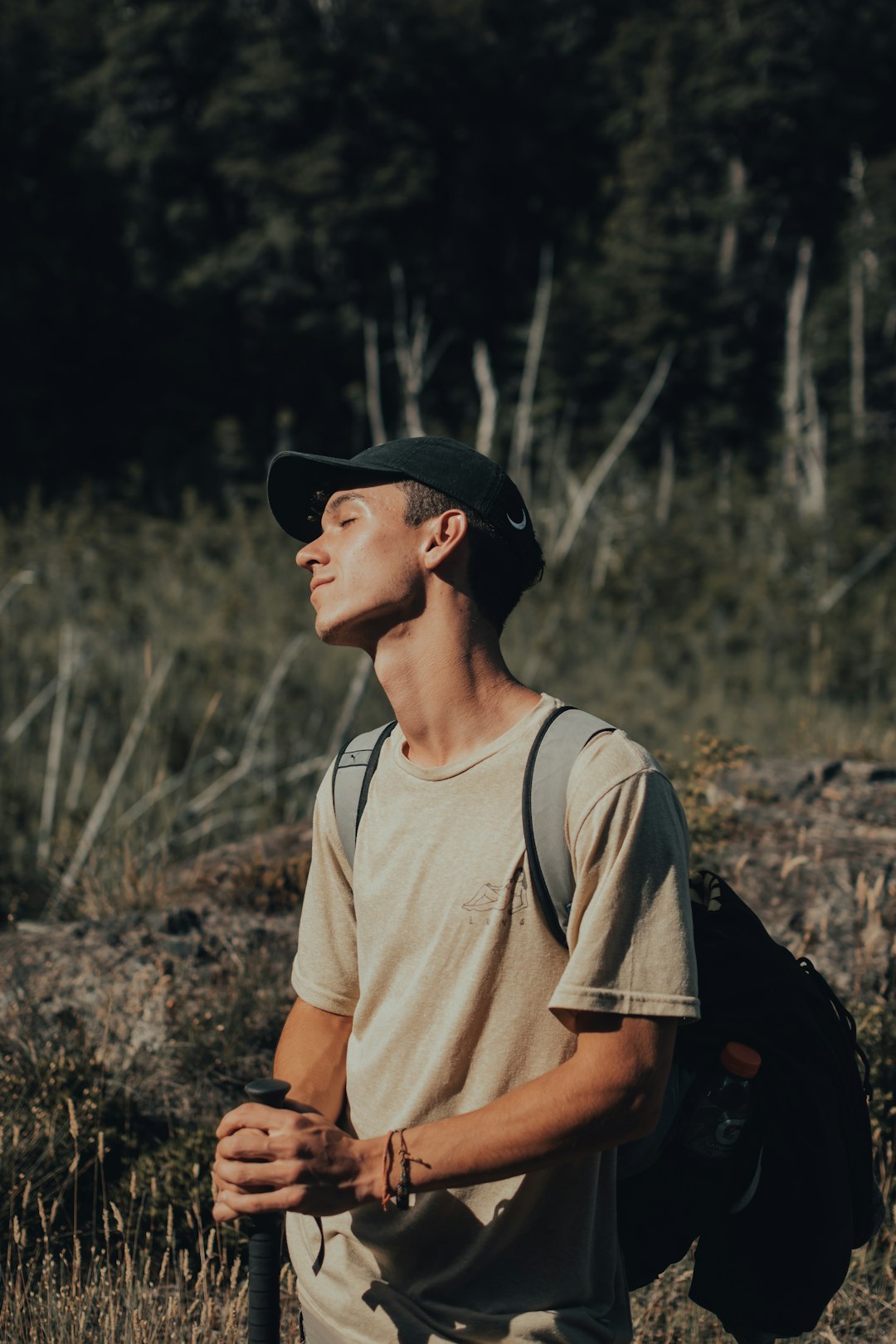 man in white crew neck t-shirt wearing black cap standing on brown grass field during