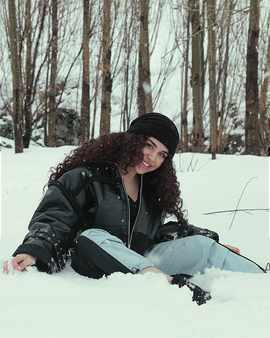 woman in black jacket and black knit cap sitting on snow covered ground during daytime