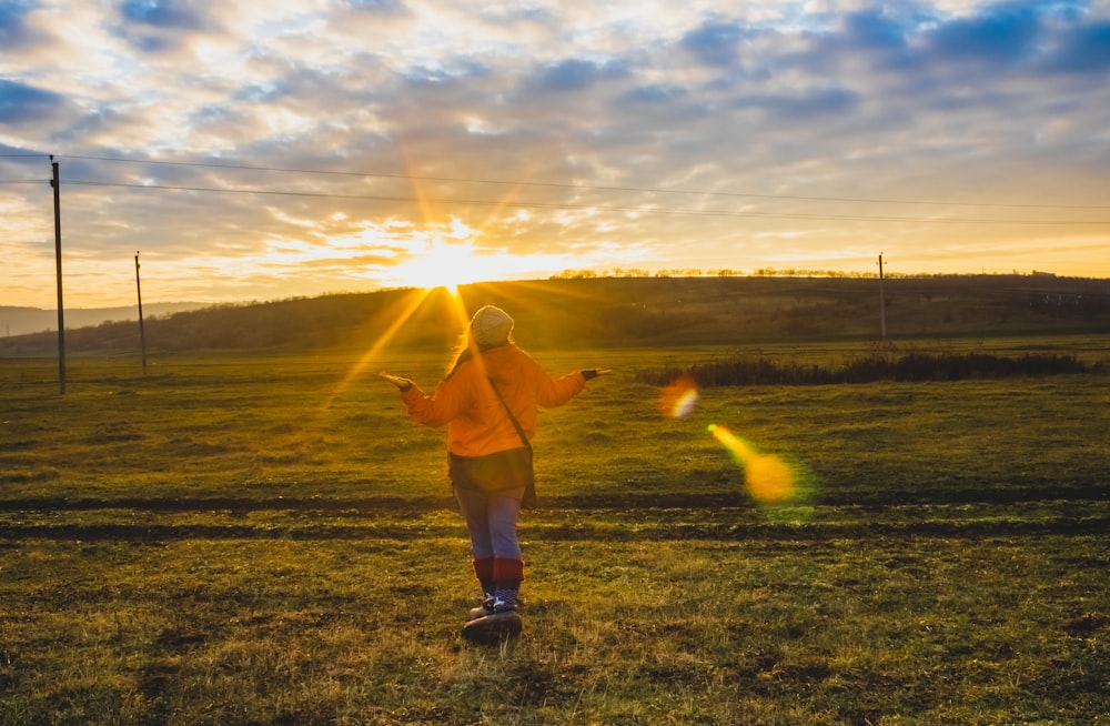 man in brown shirt and white shorts standing on green grass field during sunset