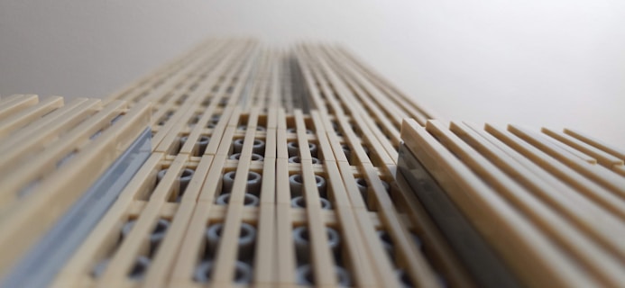 A close-up view of a structure composed of beige and light gray LEGO bricks, creating a tall, narrow design that resembles a skyscraper when viewed from a low angle.