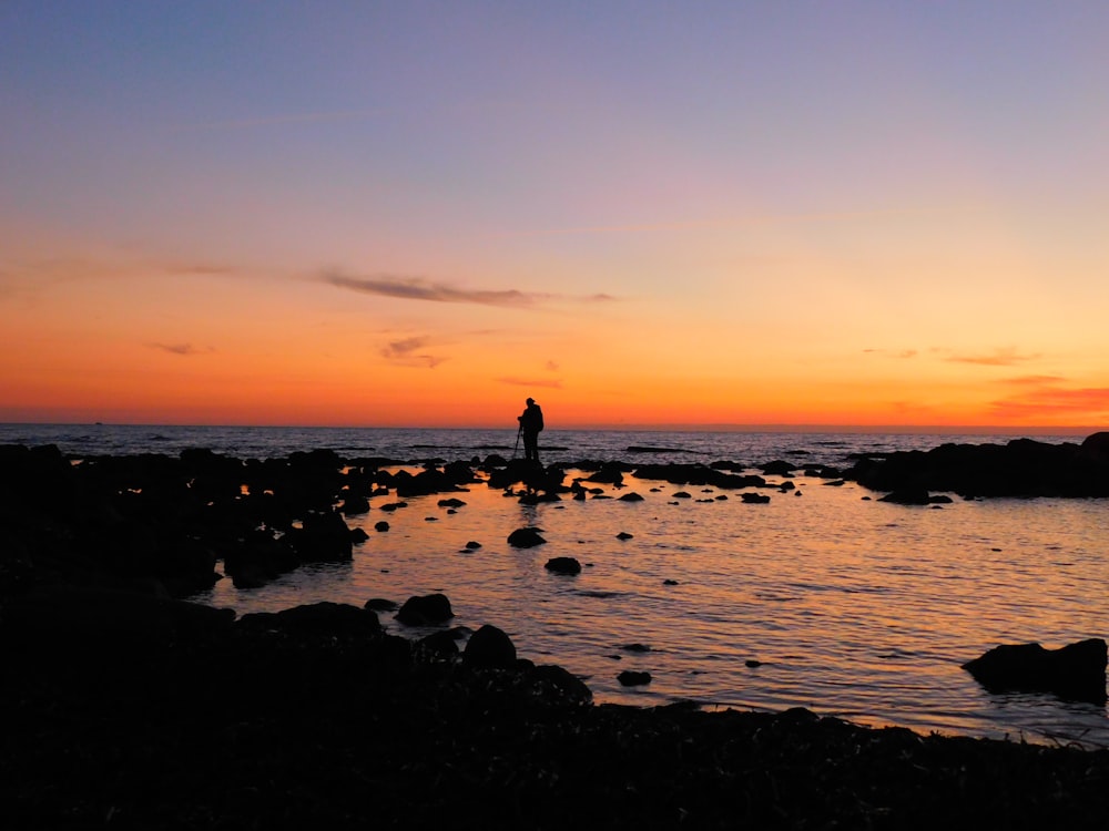 Silueta de la persona de pie en la orilla del mar durante la puesta del sol