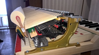 A detailed view of the internal mechanism of a piano. The image features a close-up of the hammers and strings, displaying intricate metal and wood components. The surrounding area is well-lit, emphasizing the craftsmanship and complexity of the instrument.