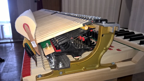 A detailed view of the internal mechanism of a piano. The image features a close-up of the hammers and strings, displaying intricate metal and wood components. The surrounding area is well-lit, emphasizing the craftsmanship and complexity of the instrument.