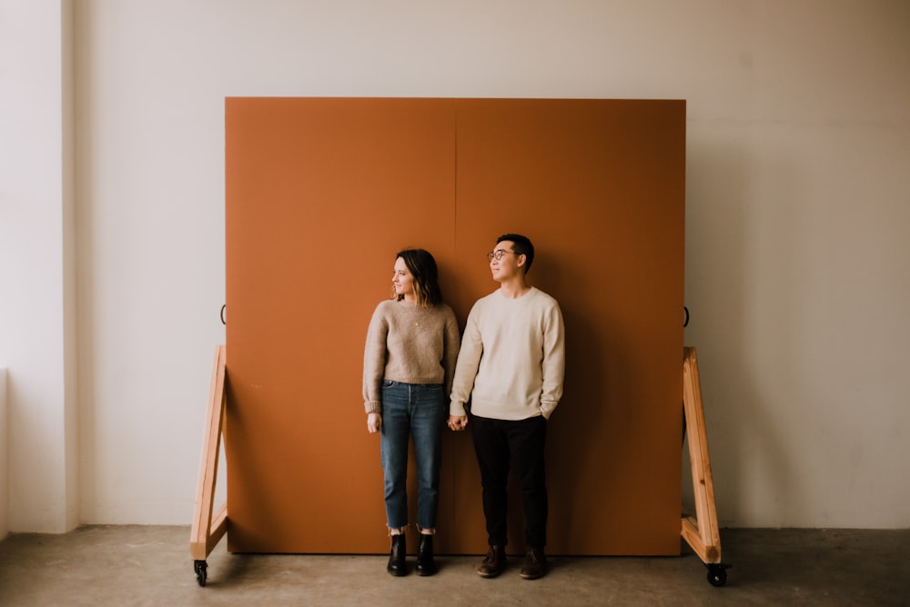 Hombre y mujer de pie junto a la pared marrón