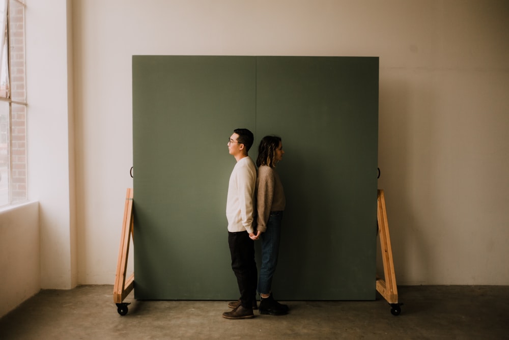 man in white dress shirt and black pants standing beside green wall