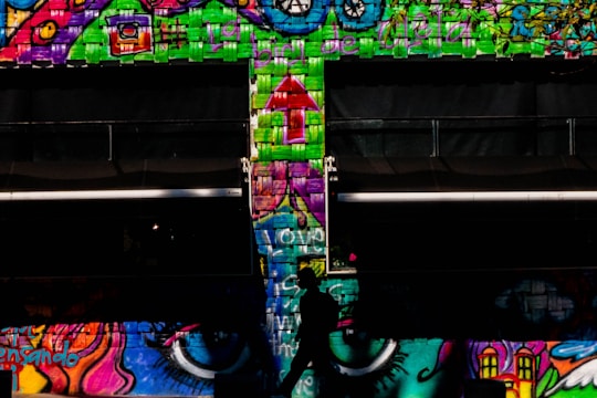 A candid street portrait of a person walking past colorful graffiti walls.