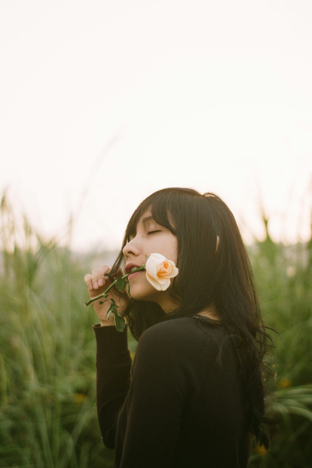 woman in black long sleeve shirt blowing white dandelion flower during daytime